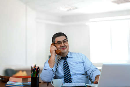 A businessman is discussing a successful deal on the phone. Smiling and looking at the camera.の写真素材