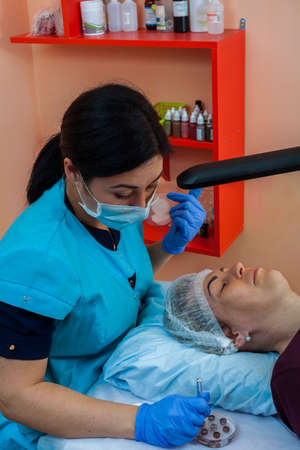 The cosmetologist performs correction of the shape of the eyebrows in the beauty salon. Semi-permanent makeup for eyebrows.の写真素材
