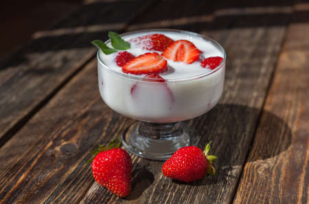 Strawberries with cream in a glass on a wooden table. Sunny summer day.の写真素材