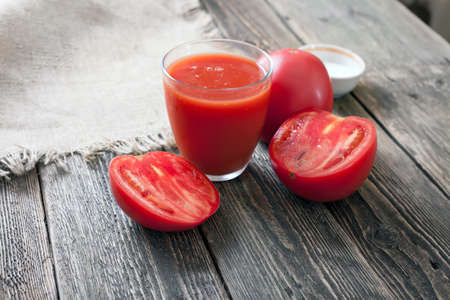 Tomato juice in a glass and slices of a tomato on a wooden table. Tomatoes and juice on wooden boards.の写真素材