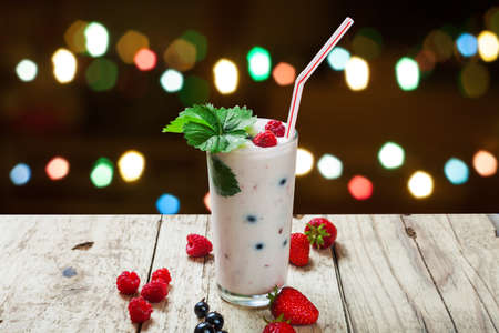 Natural fruit yogurt with berries in a glass. Beautiful festive background with bokeh. A festive dessert on a wooden table.の写真素材