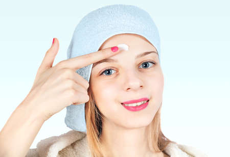 Beautiful girl puts cream on face. Photo isolated on light background.の写真素材