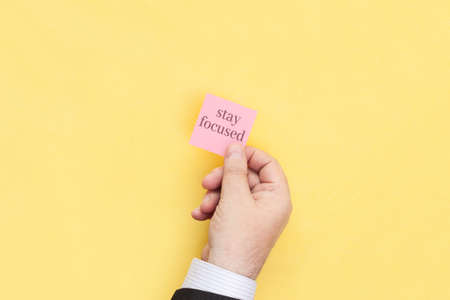 The hand holds a sticky note with inscription Stay focused. motivational statement.の写真素材