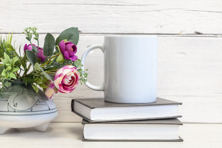 Mockup of a white ceramic mug on a table with books and flowers. White mug close up.