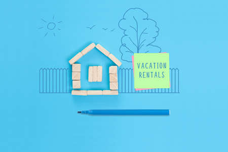 A small house made of wooden blocks and a sticky note with the words Vacation rentals. Concept photo showing short-term rental housing.の写真素材