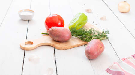 Big red tomato, potatoes, sweet peppers and dill greens on the kitchen table. Vegetables for cooking on a cutting board.の写真素材