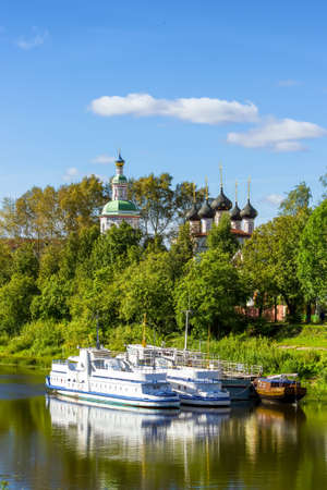 Ancient medieval Russian church on the bank of the river. Belfry and domes with crosses against the sky and greenery.の写真素材