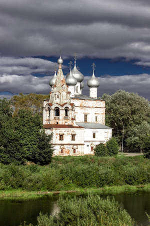 Ancient medieval Russian church on the bank of the river. Belfry and domes with crosses against the backdrop of a stormy sky.の写真素材
