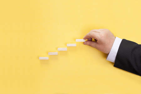 Businessman buildings a ladder from wooden blocks. Adding a wooden step to a staircase.の写真素材