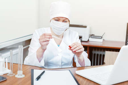 A female doctor in a white coat and mask works with blood tests. Study of blood tests in the laboratory.の写真素材