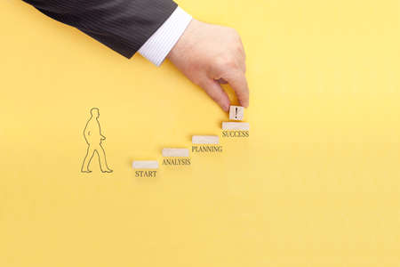 A businessman's hand is adding a wooden cube with an exclamation mark to the top rung of a ladder from business concepts. Conceptual image of setting business goals.の写真素材