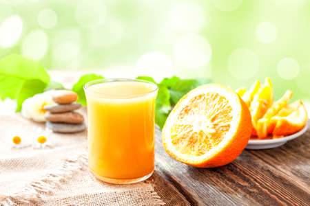 orange juice. A glass of orange juice and a ripe orange on a table against a background of greenery.の写真素材
