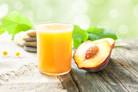 Peach juice. A glass of peach juice and a ripe juicy peach on the table against the backdrop of greenery.の写真素材