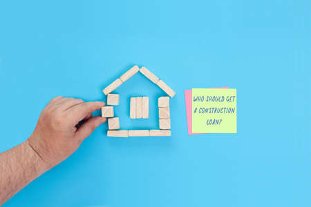 A small house made of wooden blocks and sticky notes with the words Who should get a construction loan.の写真素材