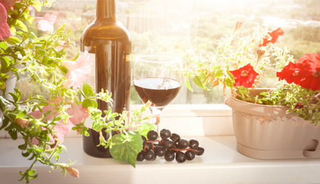 A bottle of red wine and a glass of wine are placed on a sunlit windowsill. Ideal for content about summer relaxation in Italy or Spain.の写真素材