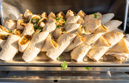 Lavash rolls with filling, laid out on a tray, illuminated by the warm light of the setting sun. A traditional snack - savory burritos.の写真素材