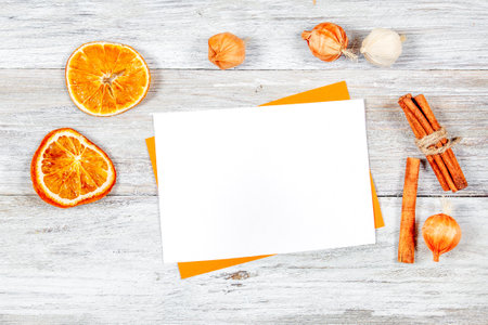 Blank white card mockup on wooden background decorated with dried orange slices and cinnamon sticks. Perfect for showcasing invitation designs for a cooking party.の写真素材