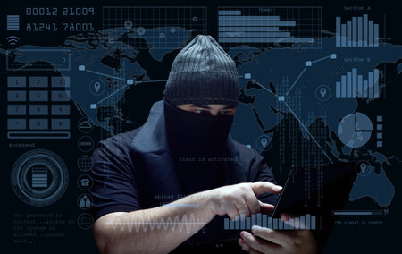A masked hacker wearing a beanie operates a laptop,surrounded by a digital HUD interface with binary code, graphs, and a world map.The scene represents cybersecurity threats,hacking and data breaches.の写真素材