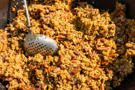Hot pilaf with meat, rice, and spices in a large metal cauldron. Close-up. Outdoor cooking at a street food market.の写真素材