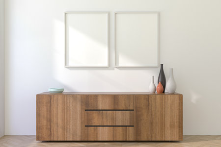 Two vertical white picture frames on a light wall above a cabinet, presented as a mockup for artwork or poster display. 3D render.の写真素材