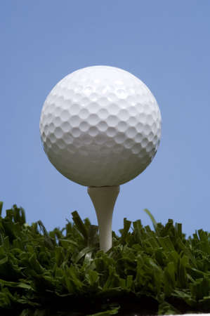 golf ball on tee on grass with blue skyの写真素材