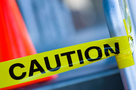 Yellow caution tape on stair rail with orange traffic cone behind, very shallow depth of field.の写真素材