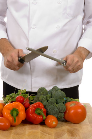 Professional chef sharpening knife inlcluding assorted fresh vegetablesの写真素材