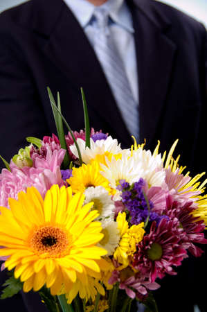 Man in blue suit presenting an arrangement of springtme flowersの写真素材