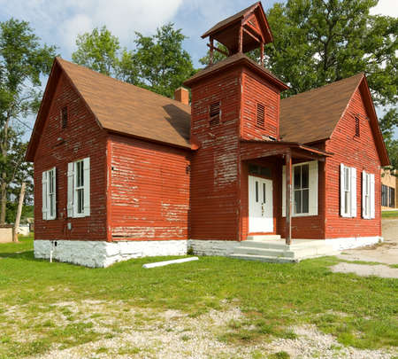 Old red school house with chipping paint and trees agianst blue skyの写真素材