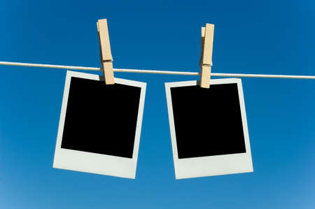 Instant transfer pictures or polaroids hanging on a clothesline with clothespins against a blue skyの写真素材