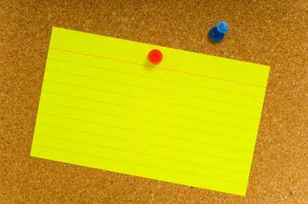Bright, blank neon colored notecards on brown corkboard or bulletin board with plastic pushpins,...