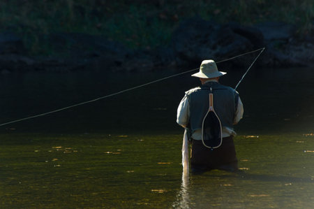 Lone fisherman with fishing pole and waders fishing in a river on beautiful sunny day