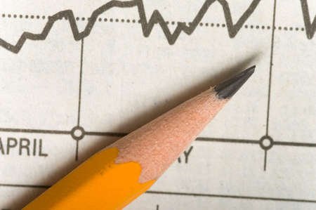 A yellow wooden pencil lying on top of a stock chart or chart showing a upward trend, illustrates studying the markets or business charts etcの写真素材