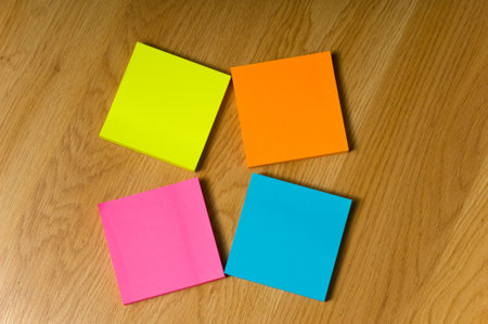Several blank neon colored post-it notes lying on a wooden floor or desk