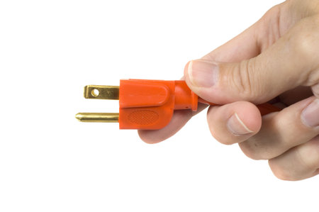 A man's hand holding the end of a new orange extension cord on a white background, symbol for connection or getting connected or plugged inの写真素材