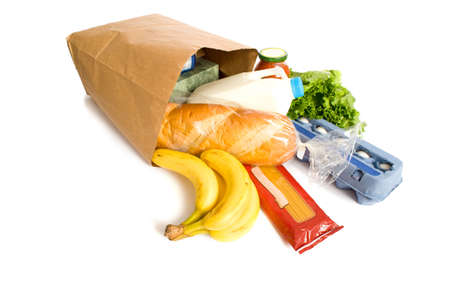 A brown paper bag full of groceries on a white background, with bread, milk, eggs, pasta, lettuce and bananas.  with copy spaceの写真素材