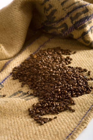Roasted Coffee beans lying on top of a brown burlap coffee bean transportation bagの写真素材