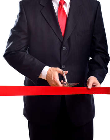 A business man wearing a blue suit cutting a red ribbon with a pair of shiny silver scissors.  Grand opening ceremony or eventの写真素材