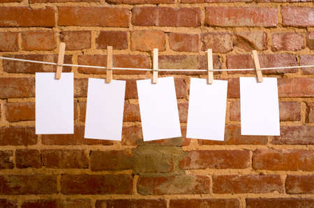 A row of five blank notes on clothesline in front of a brick wall, with copy spaceの写真素材