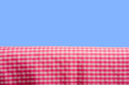 A background consisting of a pink gingham tablecloth on a blue sky background with copy spaceの写真素材