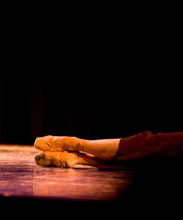 A performer laying on a stage under stage lighting with well worn ballet shoes, some noise in imageの写真素材