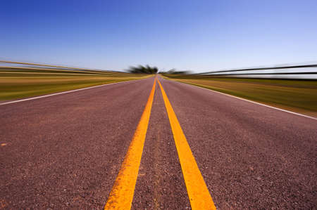 A long road bordered by farm fences and telephone wire against a blue skyの写真素材