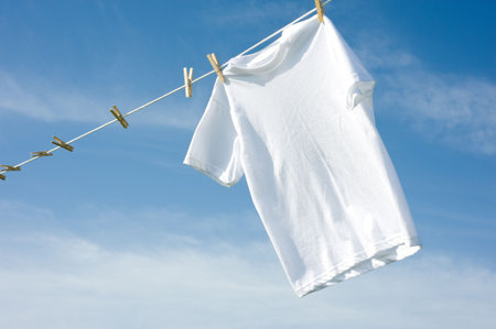 A plain white T-shirt hanging on a clothesline on a beautiful, sunny day, add text or graphic to...