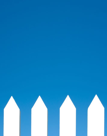 A white picket fence background in front of a bright blue sky with copy space.の写真素材