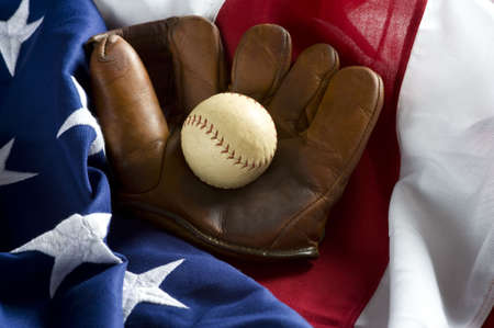 A grouping of classic baseball items including an anitque glove or mitt and an antique baseball on top of an American Flagの写真素材