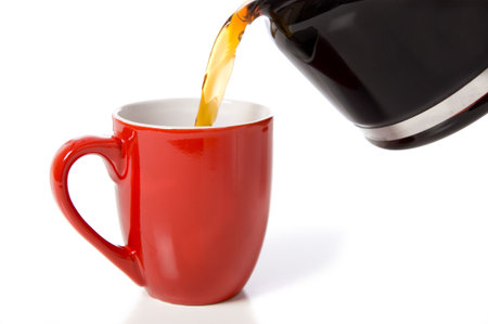 Pouring a cup of coffee into a red china or porcelain cup on a white background with copy spaceの写真素材