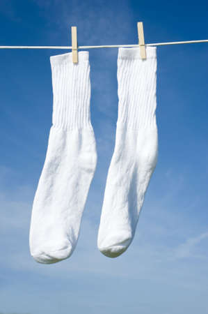 A pair of white socks on a clothesline in front of a blue sky with clothespinsの写真素材
