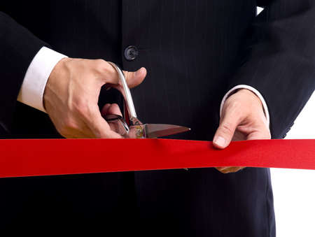 A business man wearing a blue suit cutting a red ribbon with a pair of shiny silver scissors.  Grand opening ceremony or eventの写真素材