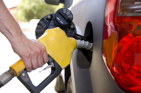 A hand holding a gasoline nozzel pumping gasoline into a car