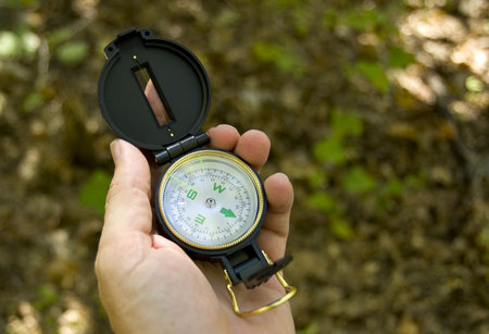 A man's hand holding an engineer's compass on a hiking trail